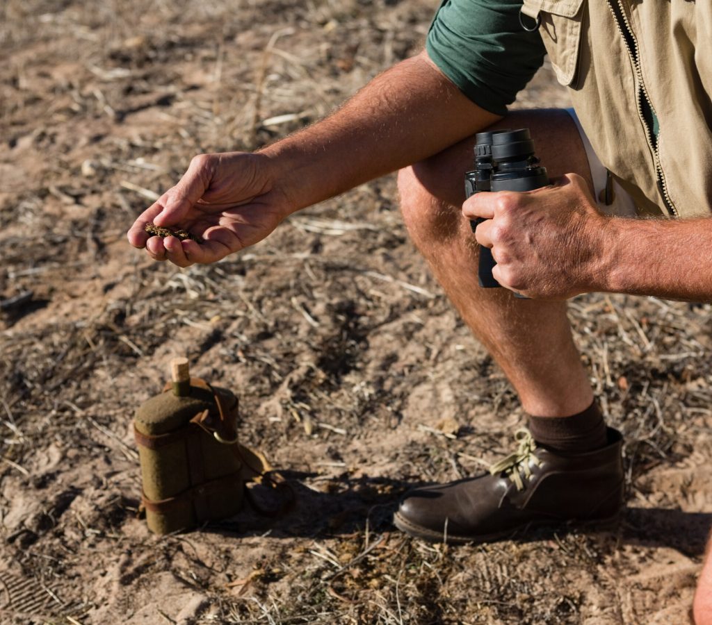 Low section of man holding mud and binocular on field